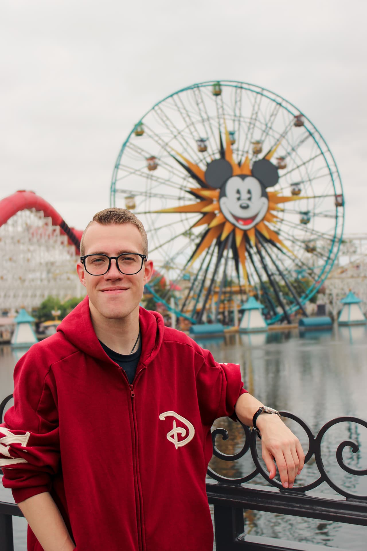 Man in a red hooded sweatshirt smiling in front of a Ferris wheel