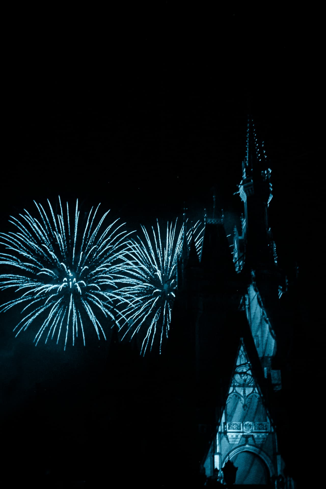 Blue fireworks bursting beside a dark castle spire at night